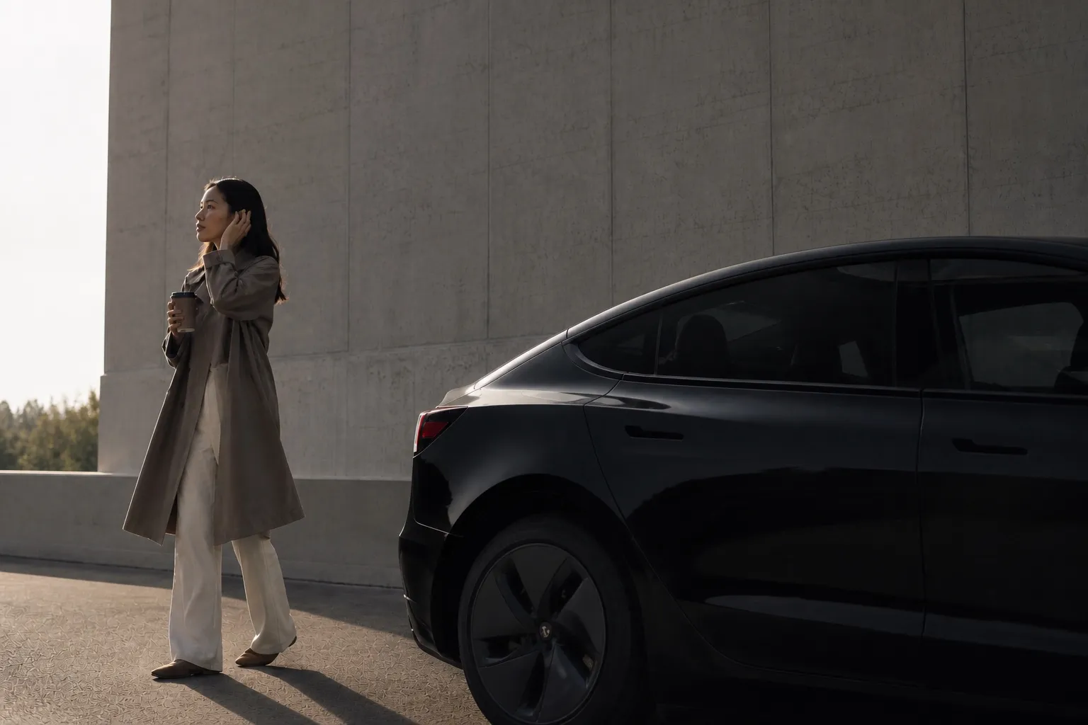 Tesla Model 3 noire stationnée devant un immeuble béton, femme avec café